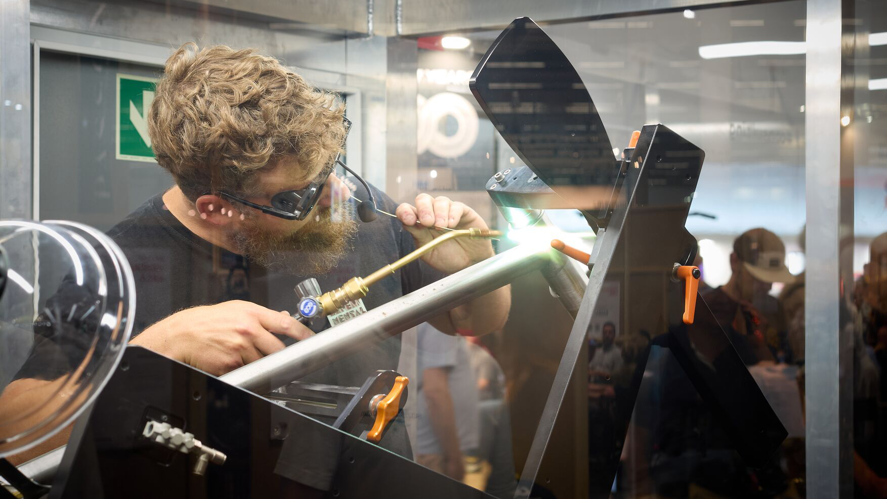Specialist demonstrating precise welding of a bicycle frame inside a glass workshop environment.