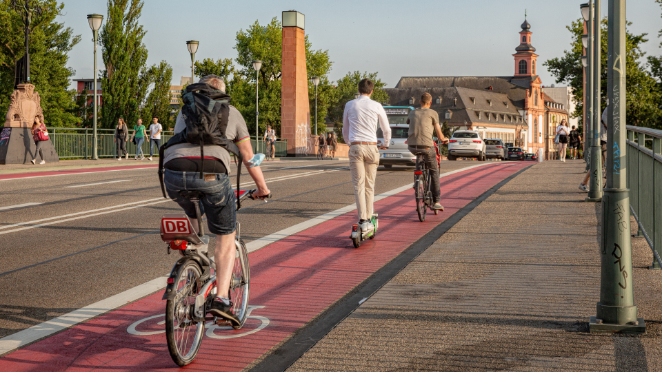 Cyclists and an e-scooter rider use a red bike lane on a city bridge.