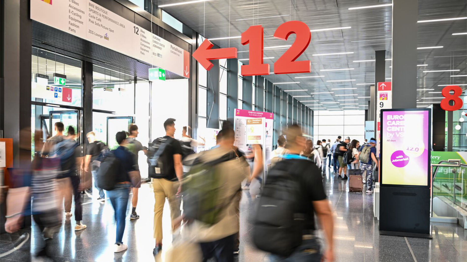 Besucherandrang in Messehalle mit Wegweisern